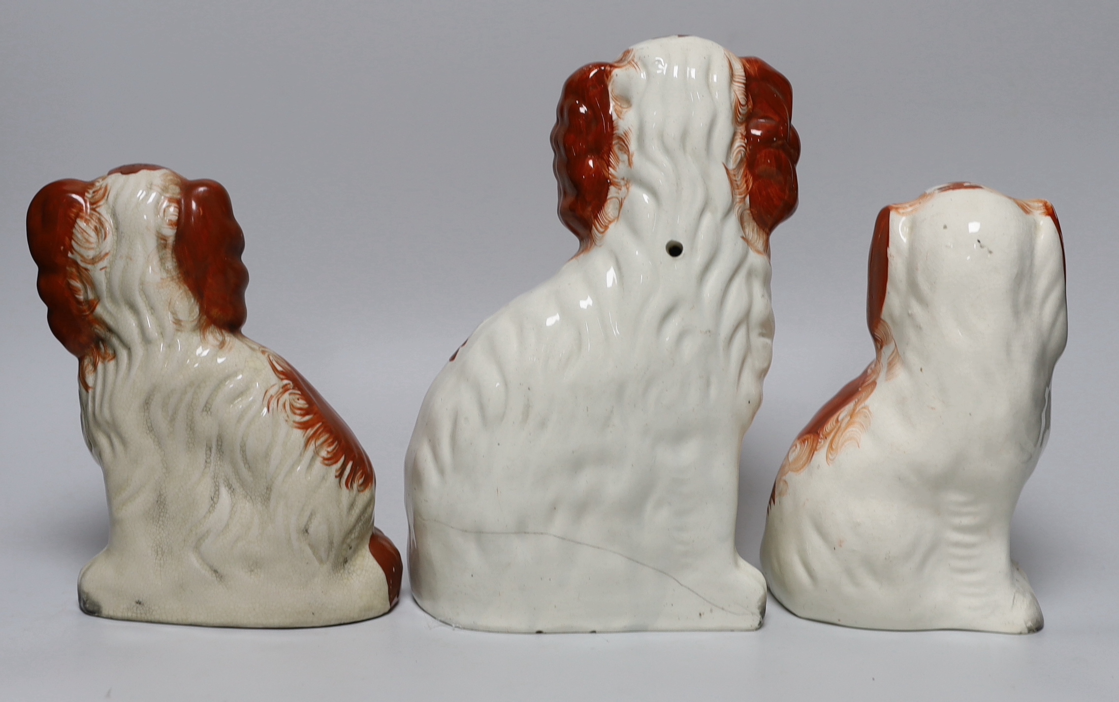 Three Victorian Staffordshire pottery dogs, one holding a basket of flowers from its mouth, the largest 24.5cm high